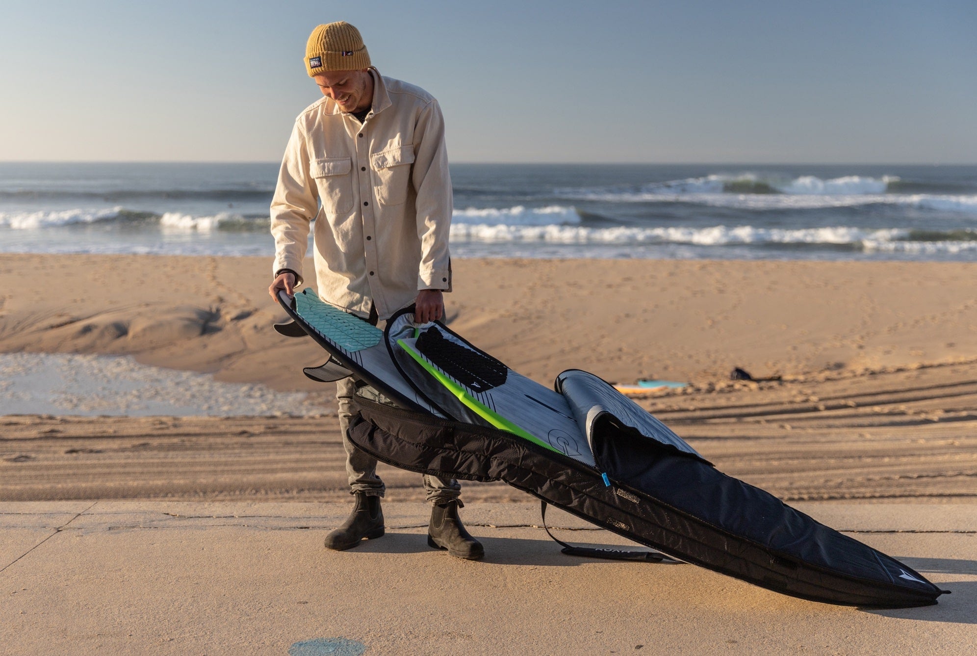 man on beach putting surfboards into a bag