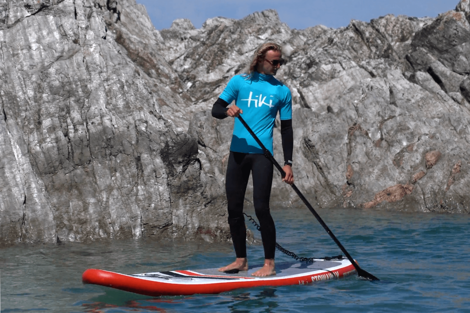 Man wearing a tiki rash vest riding on an inflatable paddleboard